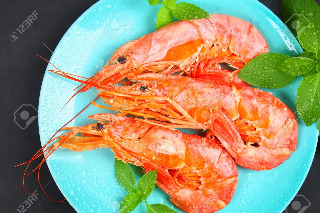 A blue plate topped with shrimp and mint leaves.