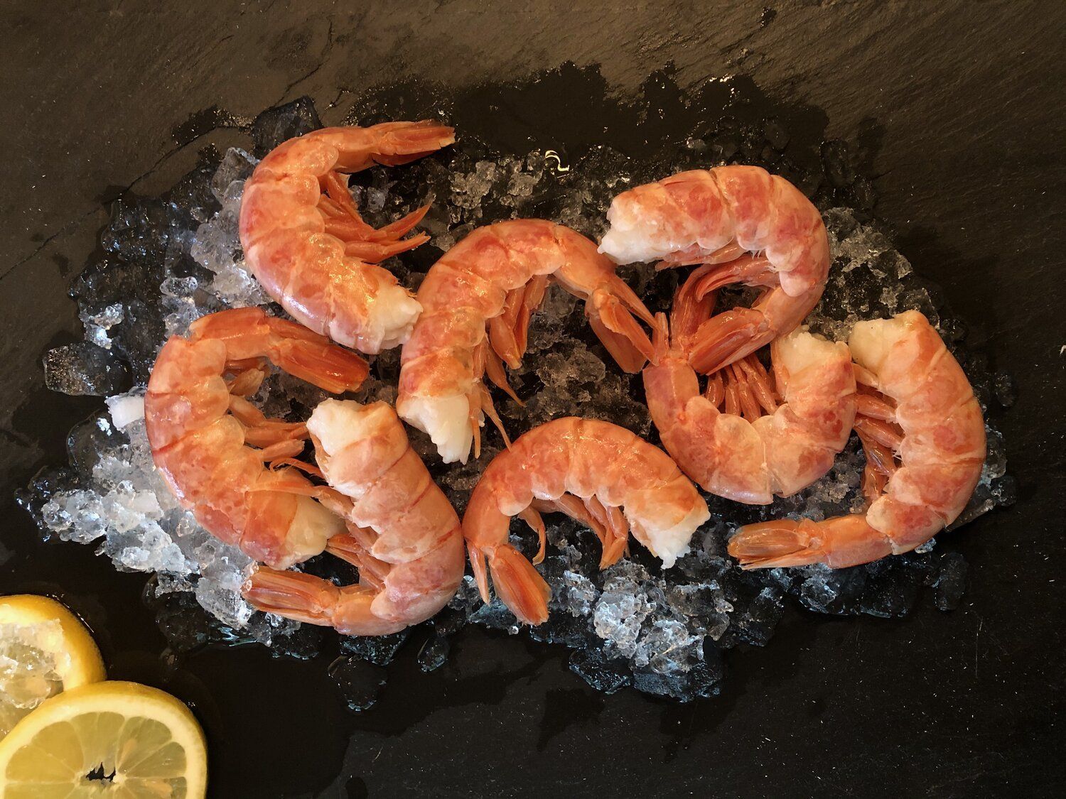 A pile of shrimp on ice with lemon slices