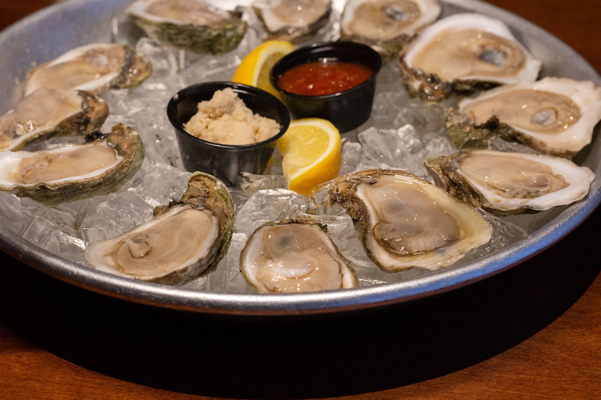 A plate of oysters on the half shell on ice with dipping sauces.