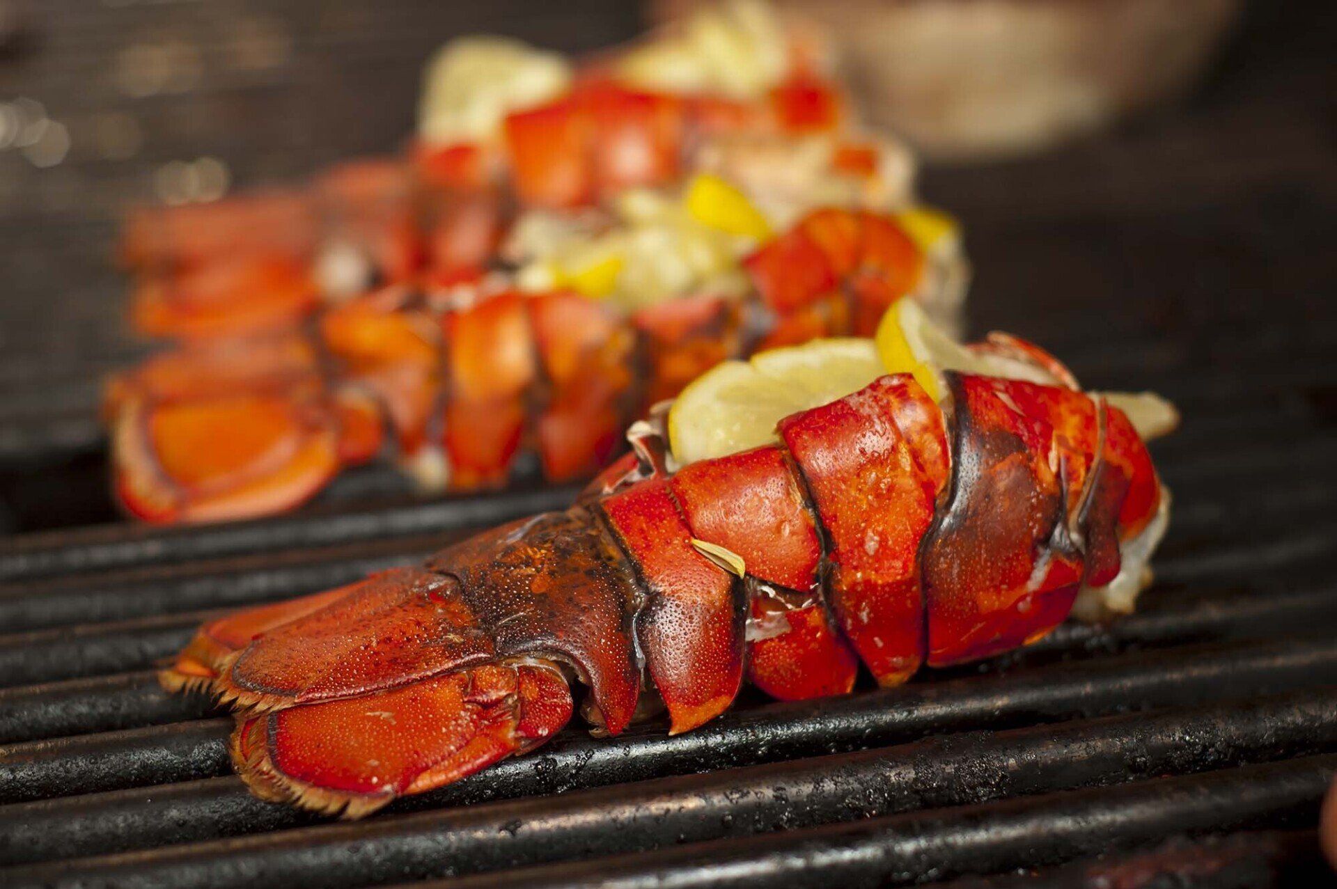 Lobsters are being cooked on a grill with lemon slices.