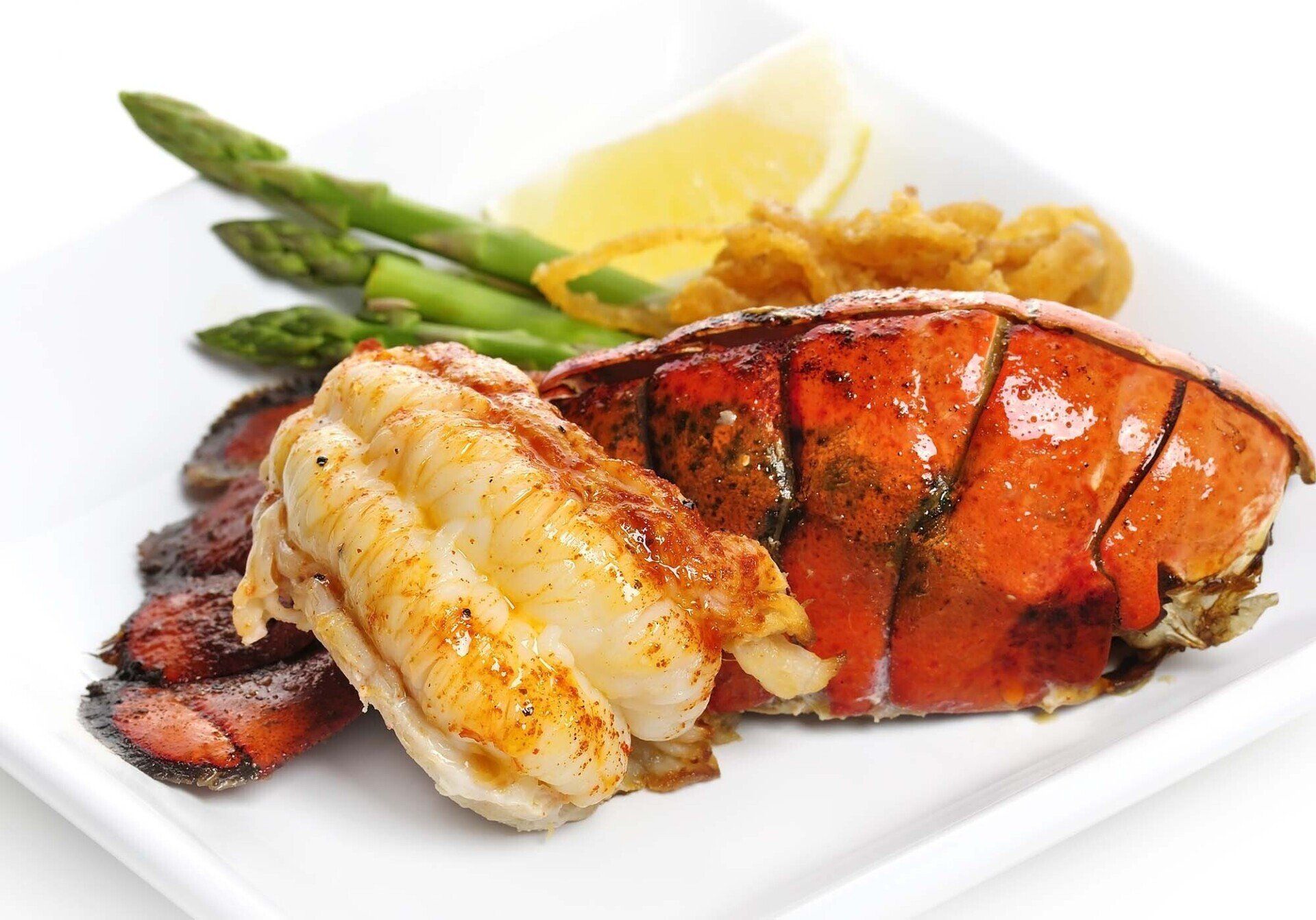 A white plate topped with lobster tails and asparagus