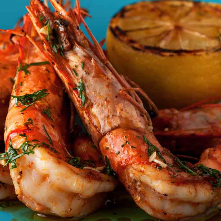 A close up of shrimp and a grilled lemon on a blue plate.