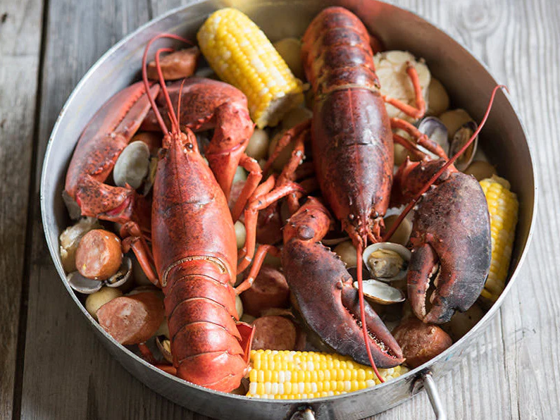 A pan filled with lobsters , corn on the cob , clams and sausage.