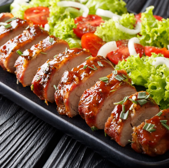 A black plate topped with meat and vegetables on a wooden table.