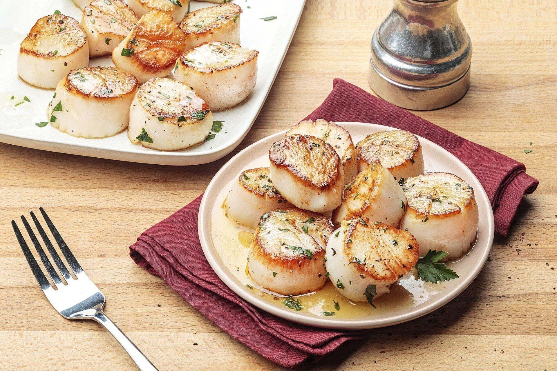 A plate of scallops with a fork on a napkin on a table.
