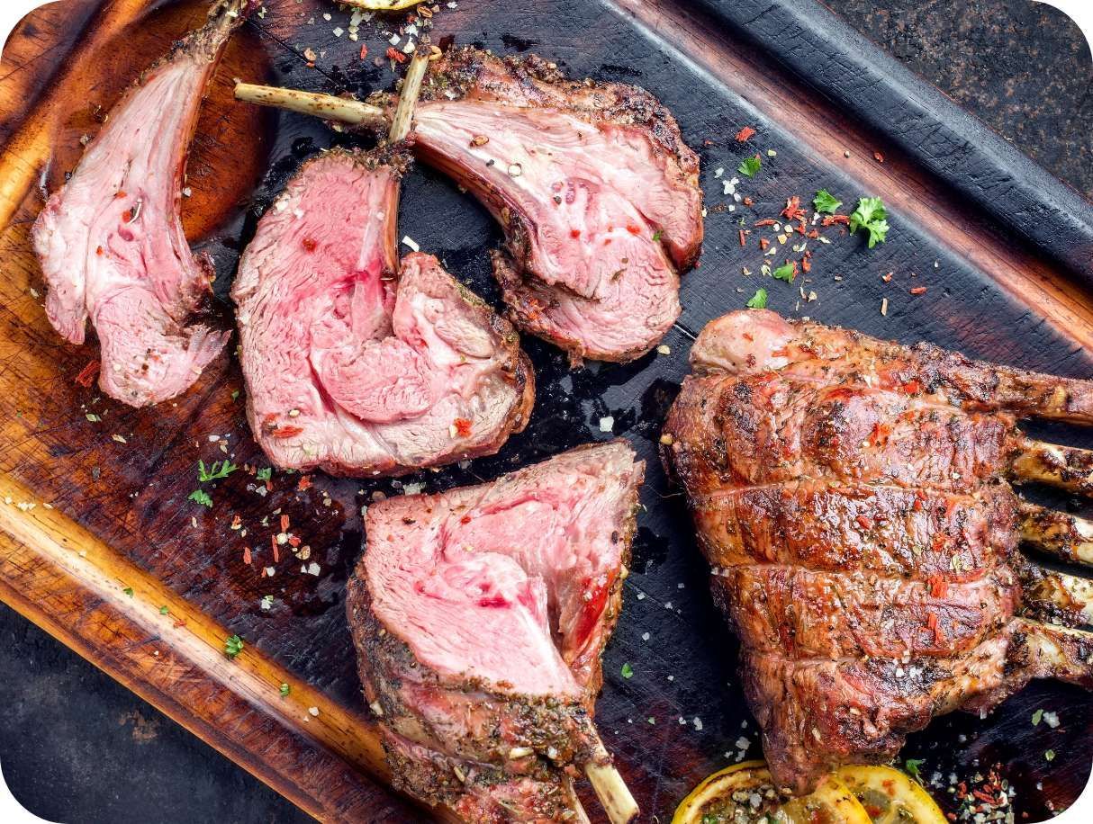 A wooden cutting board topped with sliced lamb chops.