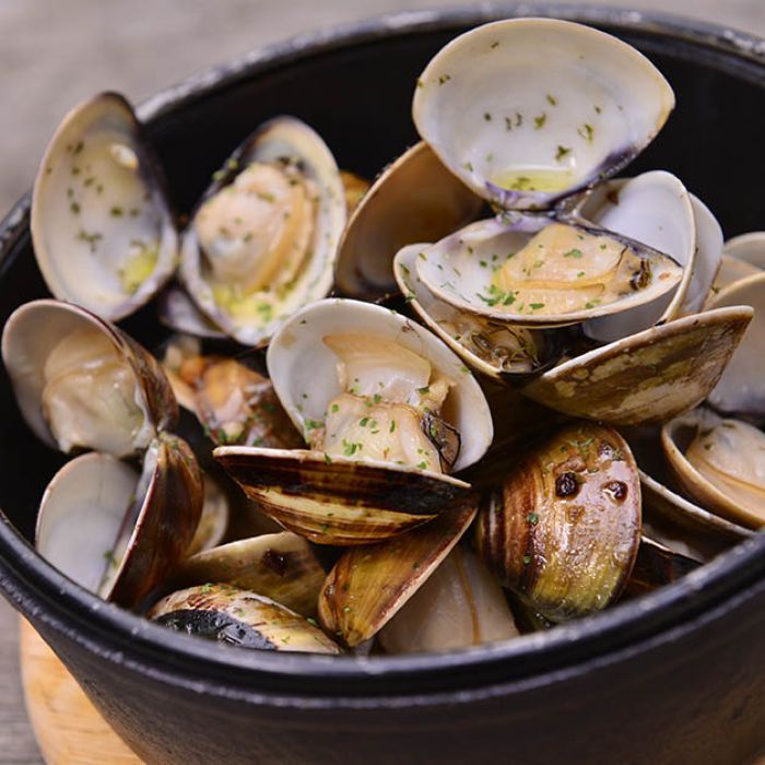 A bowl of clams is sitting on a wooden table.