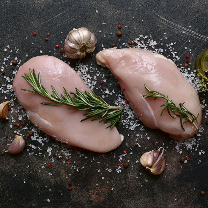 Two raw chicken breasts with garlic and rosemary on a table.