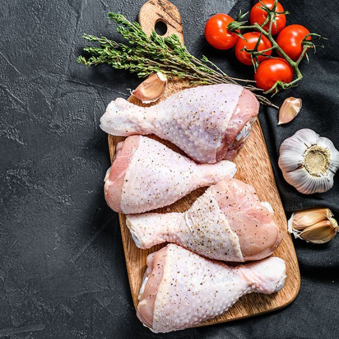 Raw chicken legs on a wooden cutting board with garlic and tomatoes.