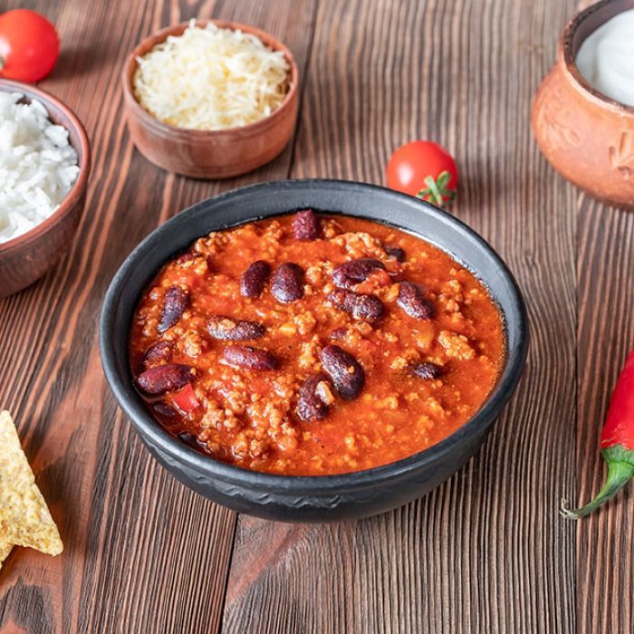 A bowl of chili is sitting on a wooden table.