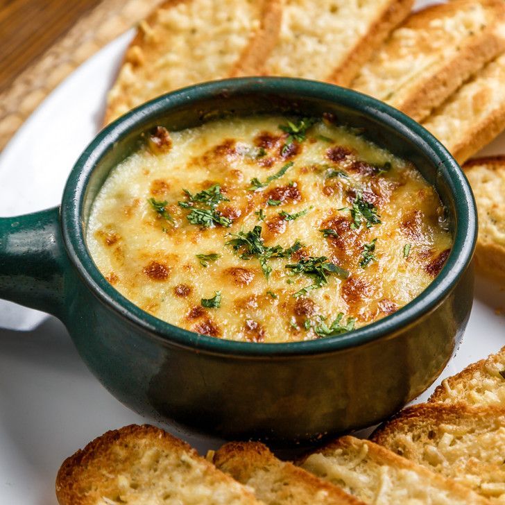 A bowl of cheese dip with garlic bread on a plate.
