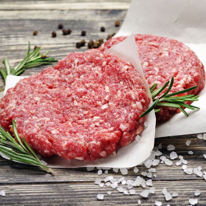 Two raw hamburger patties with rosemary and salt on a wooden table