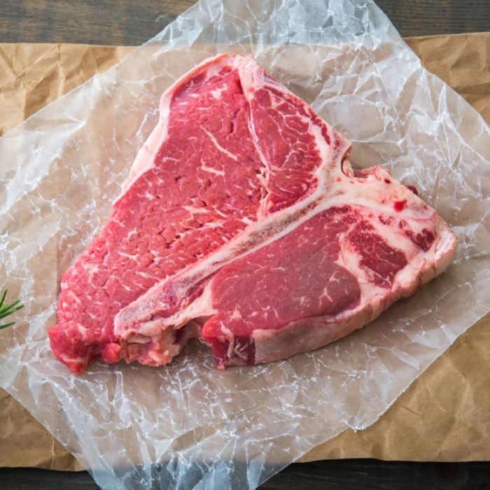 A raw t-bone steak is sitting on a piece of paper.