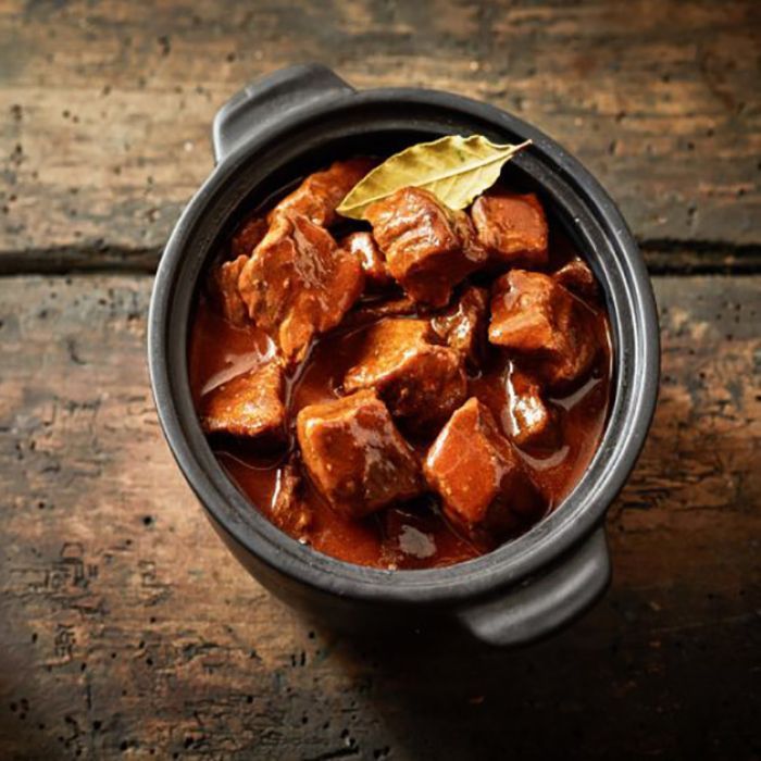 A bowl of meat stew with a bay leaf on a wooden table.