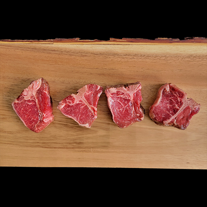 Four pieces of raw meat are sitting on a wooden cutting board.