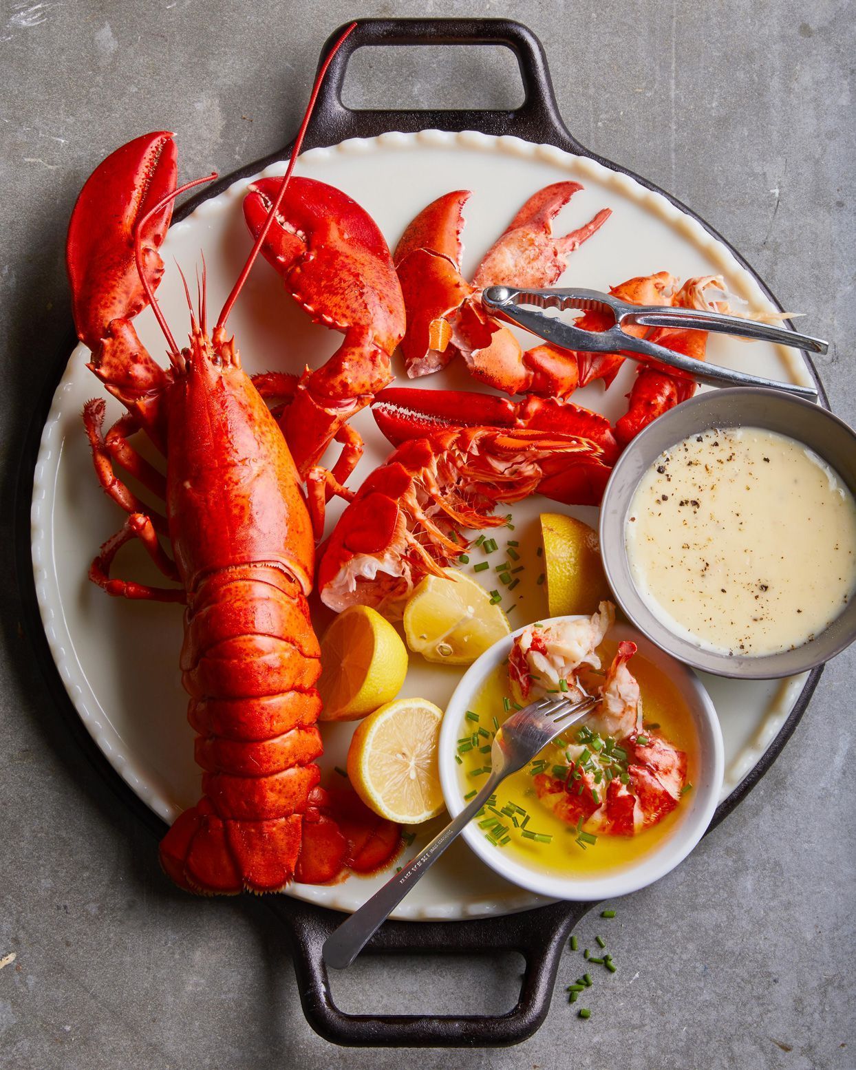 A lobster on a plate with lemons and dipping sauce