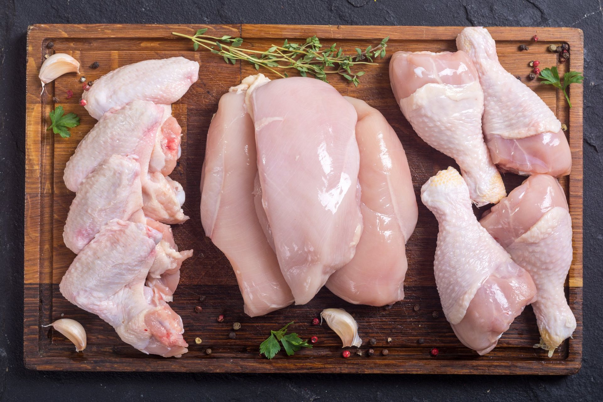 Raw chicken breasts , wings , legs and thighs on a wooden cutting board.