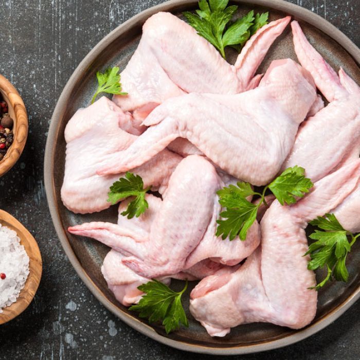 A plate of raw chicken wings with parsley on a table.