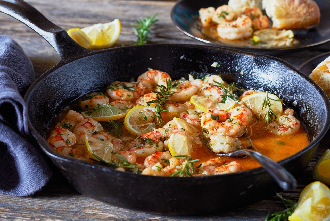 A skillet filled with shrimp and lemon slices on a table.