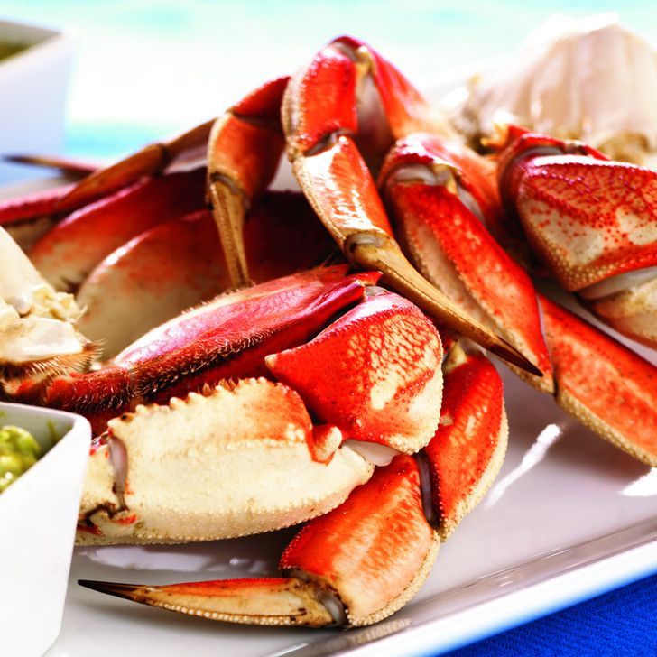 A white plate topped with crab claws next to a bowl of green peas