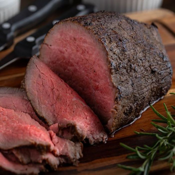 A large piece of roast beef is sitting on a wooden cutting board.