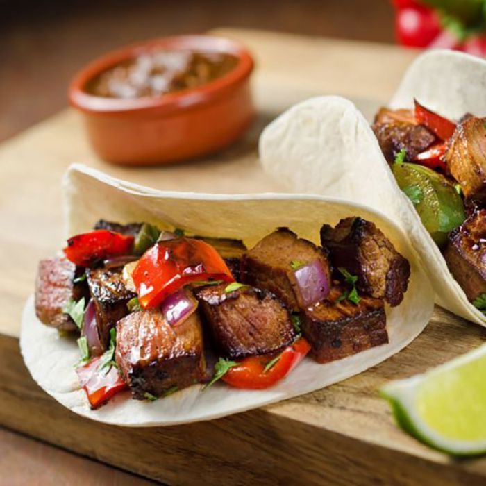 Two tacos with meat and vegetables on a wooden cutting board