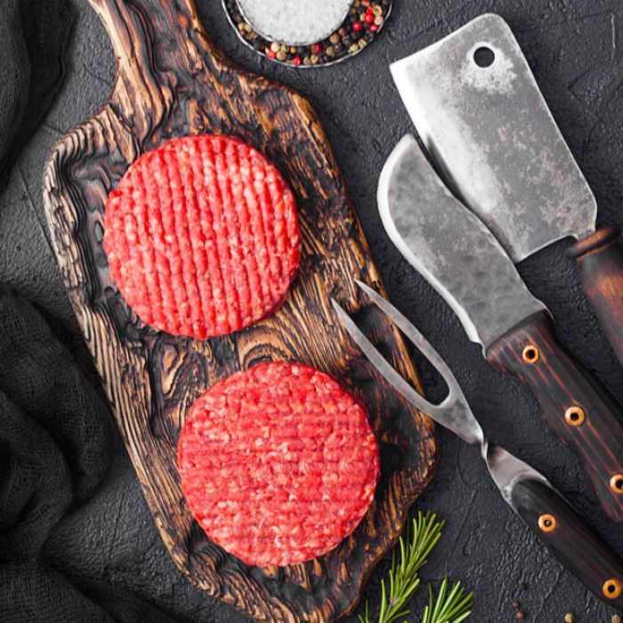 Two raw hamburger patties are sitting on a wooden cutting board.
