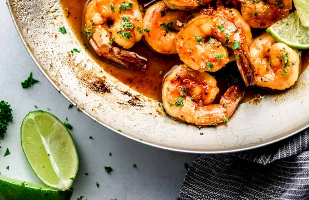 A plate of shrimp with lime wedges on a table.