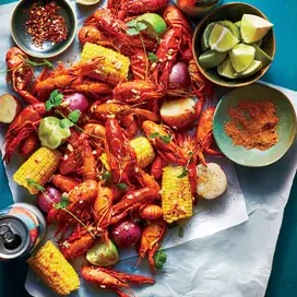 A pile of crawfish , corn , onions and other vegetables on a table.
