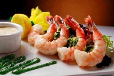 A plate of shrimp with green sauce and a yellow flower on a table.