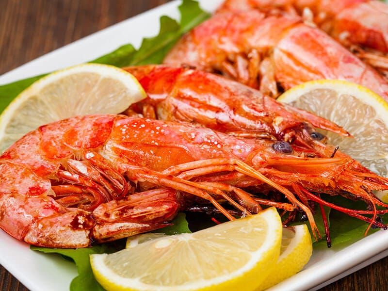A plate of shrimp with lemon slices and lettuce on a table.