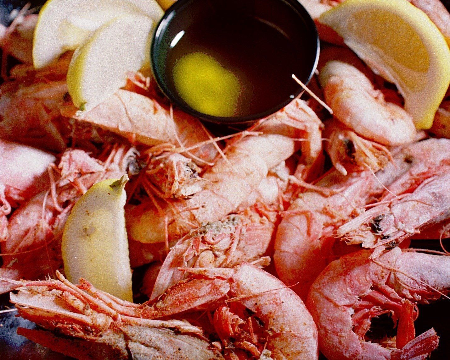 A pile of shrimp with lemon slices and a bowl of oil