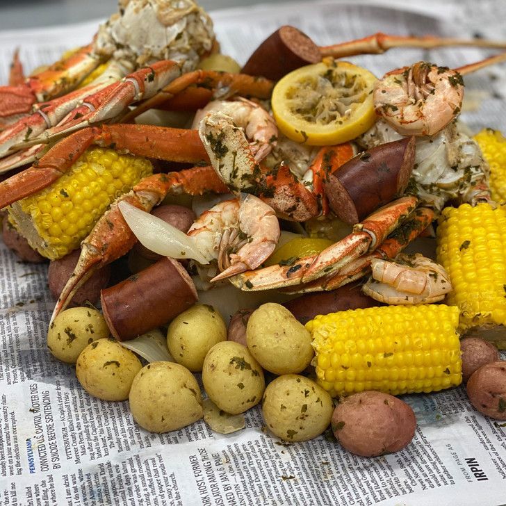 A pile of crabs , shrimp , corn , potatoes and sausage on a newspaper.