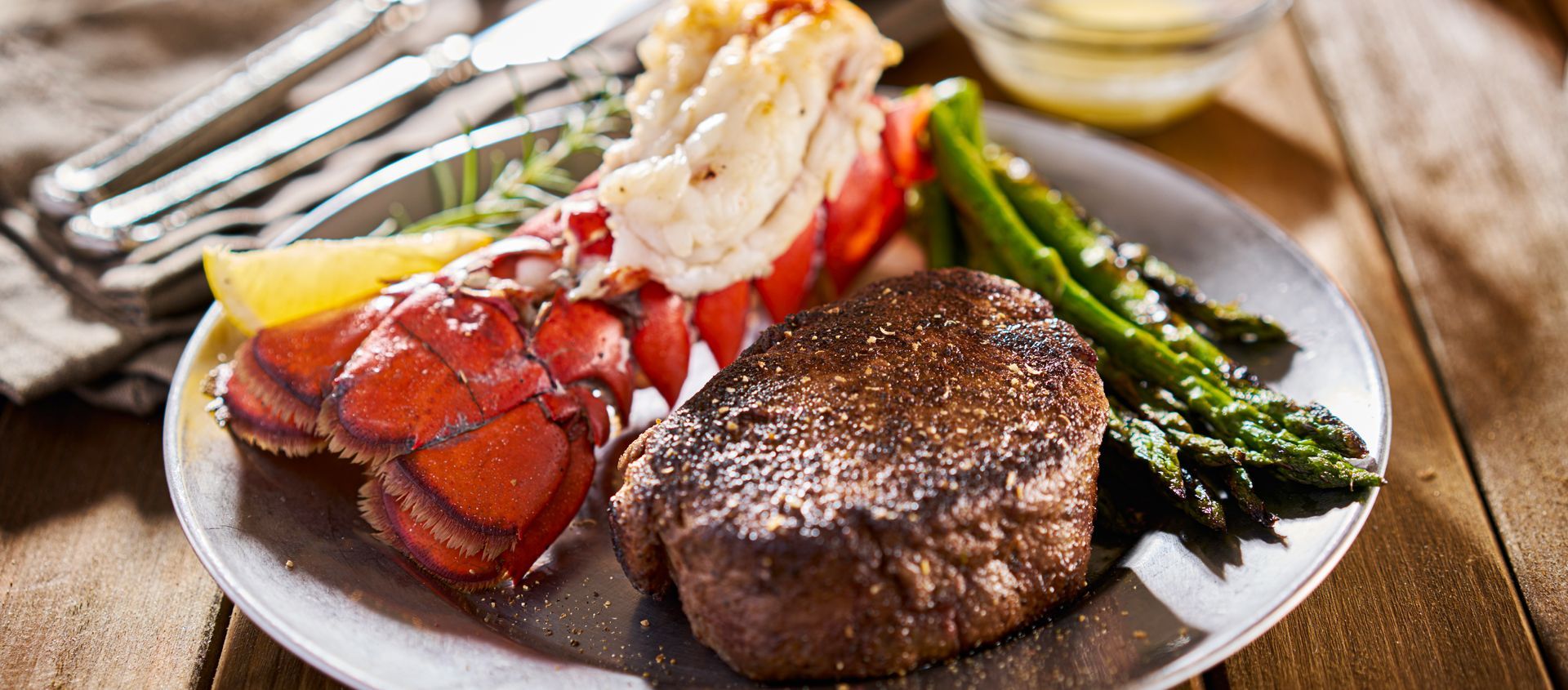 A plate of food with a steak , lobster tail , and asparagus on a wooden table.