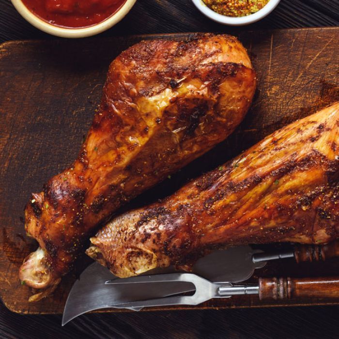 Two roasted turkey legs on a wooden cutting board