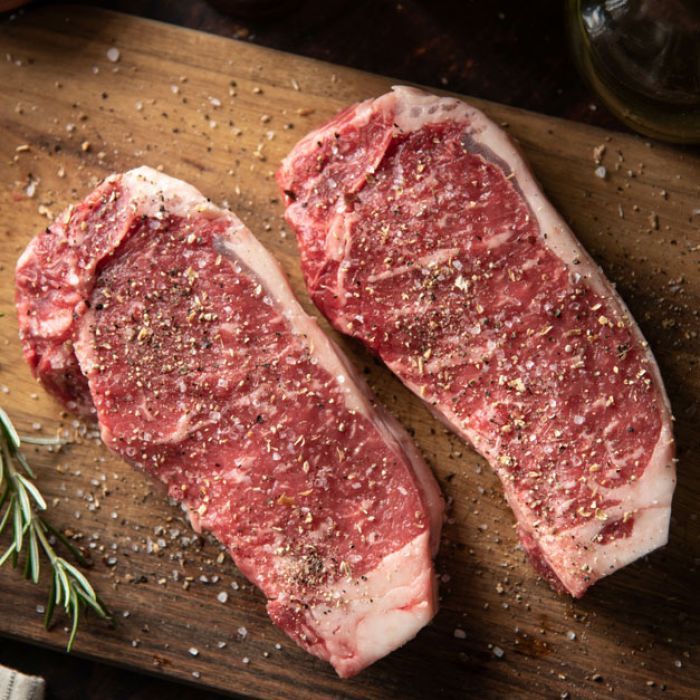 Two raw steaks are sitting on a wooden cutting board.
