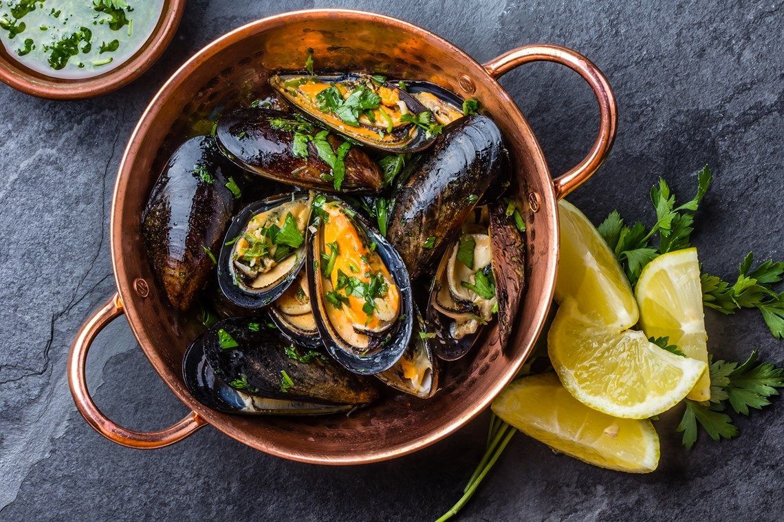 A copper pot filled with mussels and lemon slices on a table.