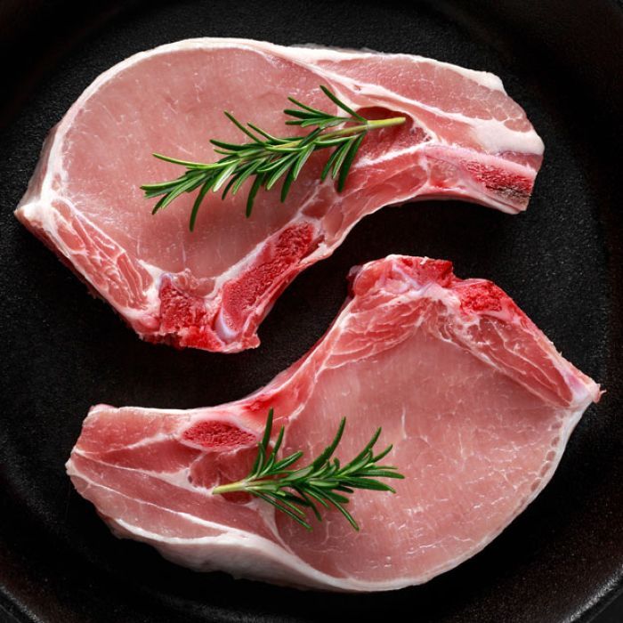 Two raw pork chops with rosemary in a skillet.