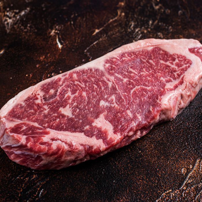A large piece of raw steak is sitting on a wooden table.