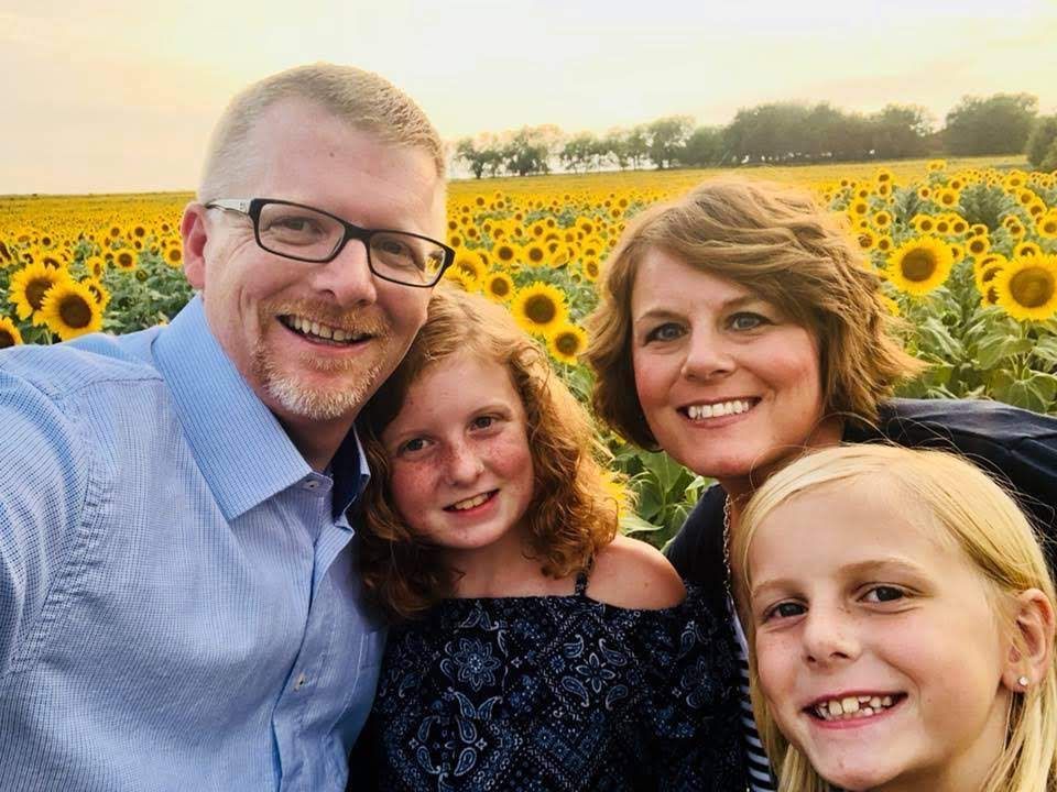 A family is posing for a selfie in front of a field of sunflowers.