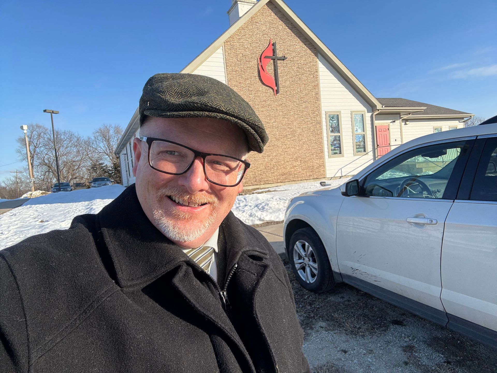 A man wearing glasses and a hat is standing in front of a church.