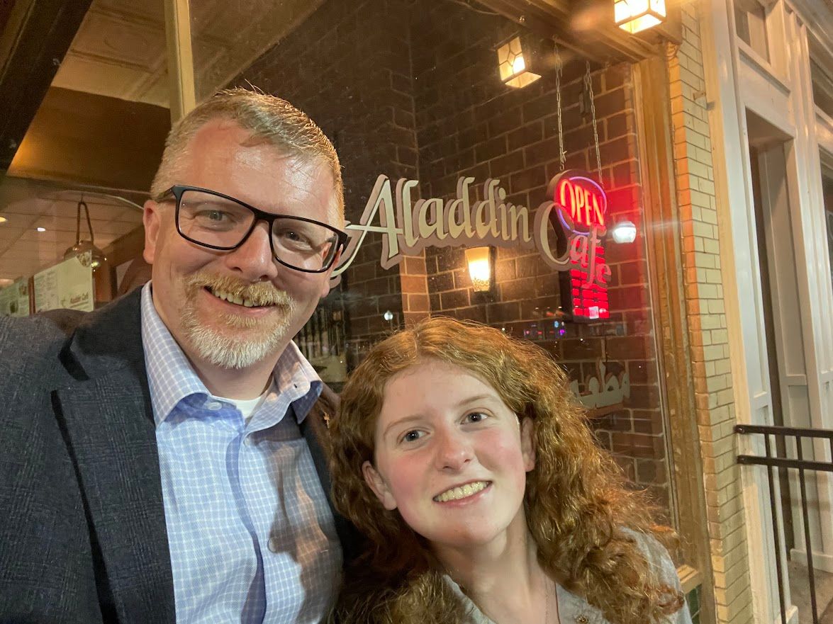 A man and a girl are posing for a picture in front of a restaurant.