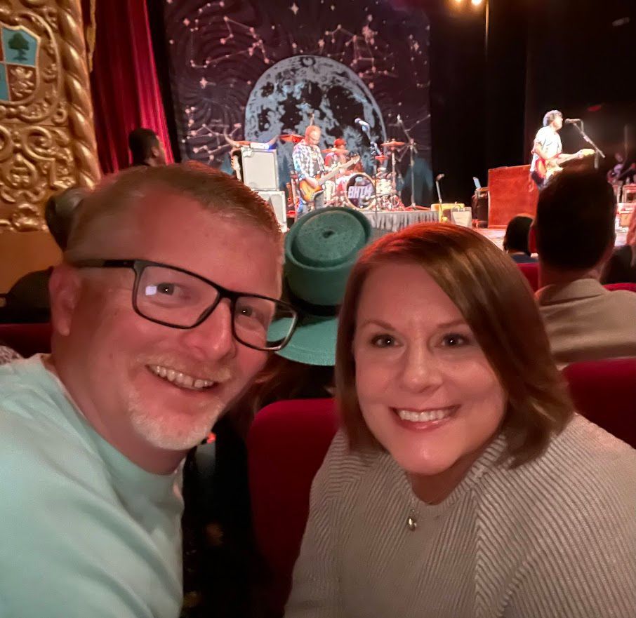 A man and a woman are posing for a picture in front of a stage