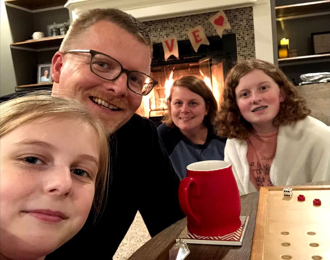 A man and three girls are taking a selfie in front of a fireplace.