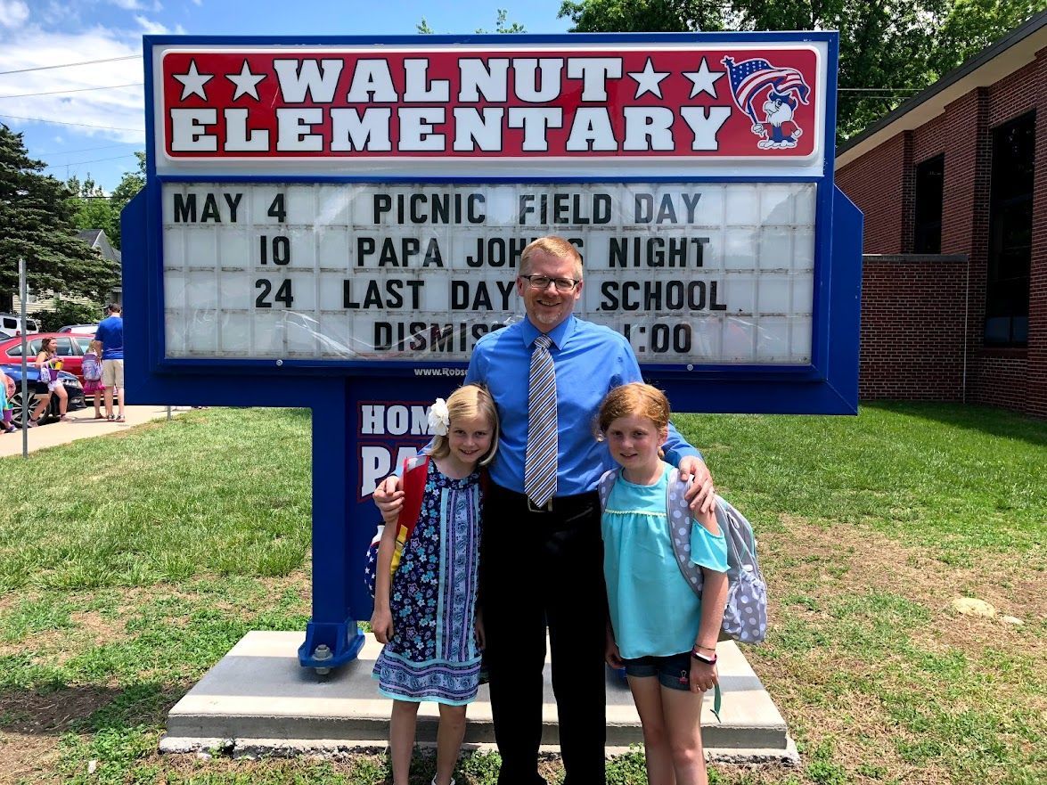 A man and two girls are standing in front of a sign for walnut elementary school.