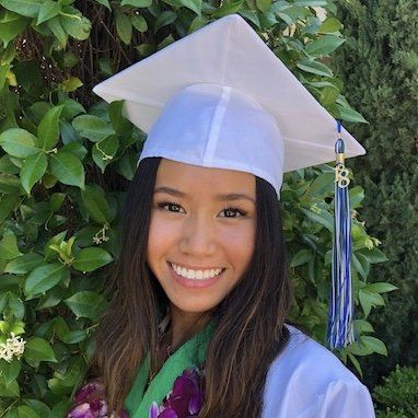 A woman wearing a white graduation cap and gown is smiling.