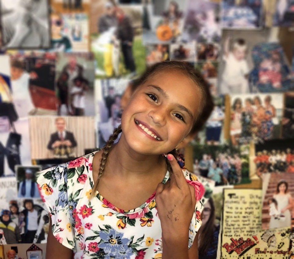 A little girl is smiling in front of a wall of pictures.