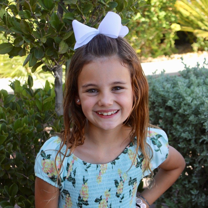 A little girl with a white bow in her hair is smiling for the camera.
