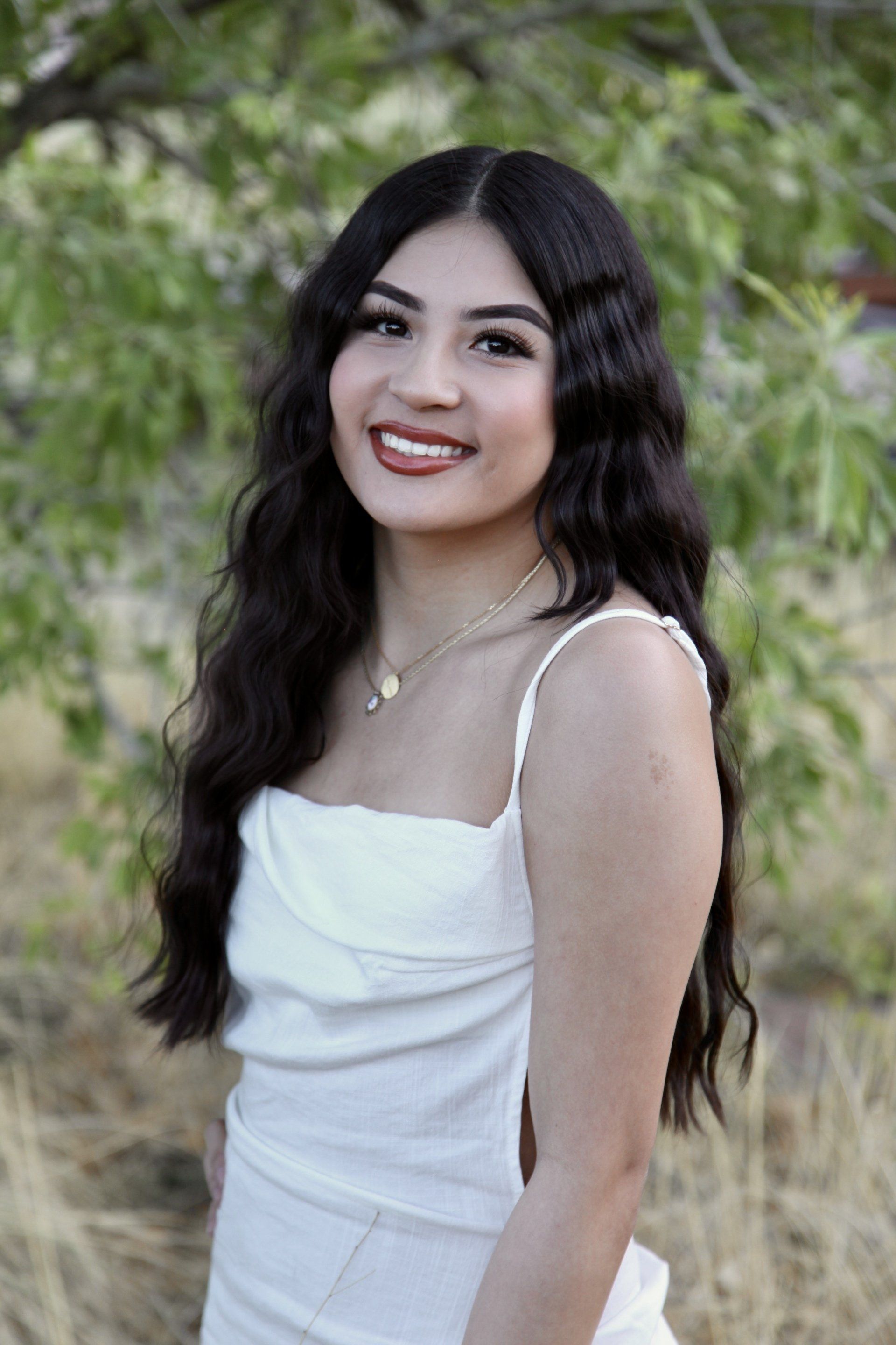 A woman in a white dress is standing in front of a tree.