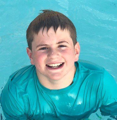 A young boy in a blue shirt is smiling in a pool
